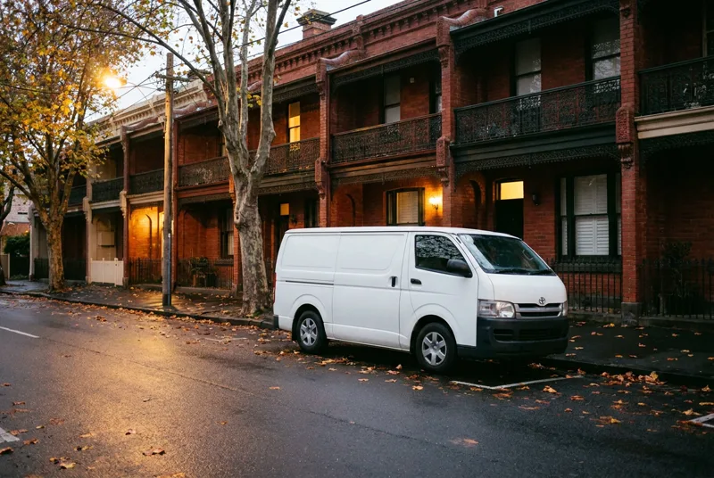 A white work van parked outside a row of brick terrace houses at dusk